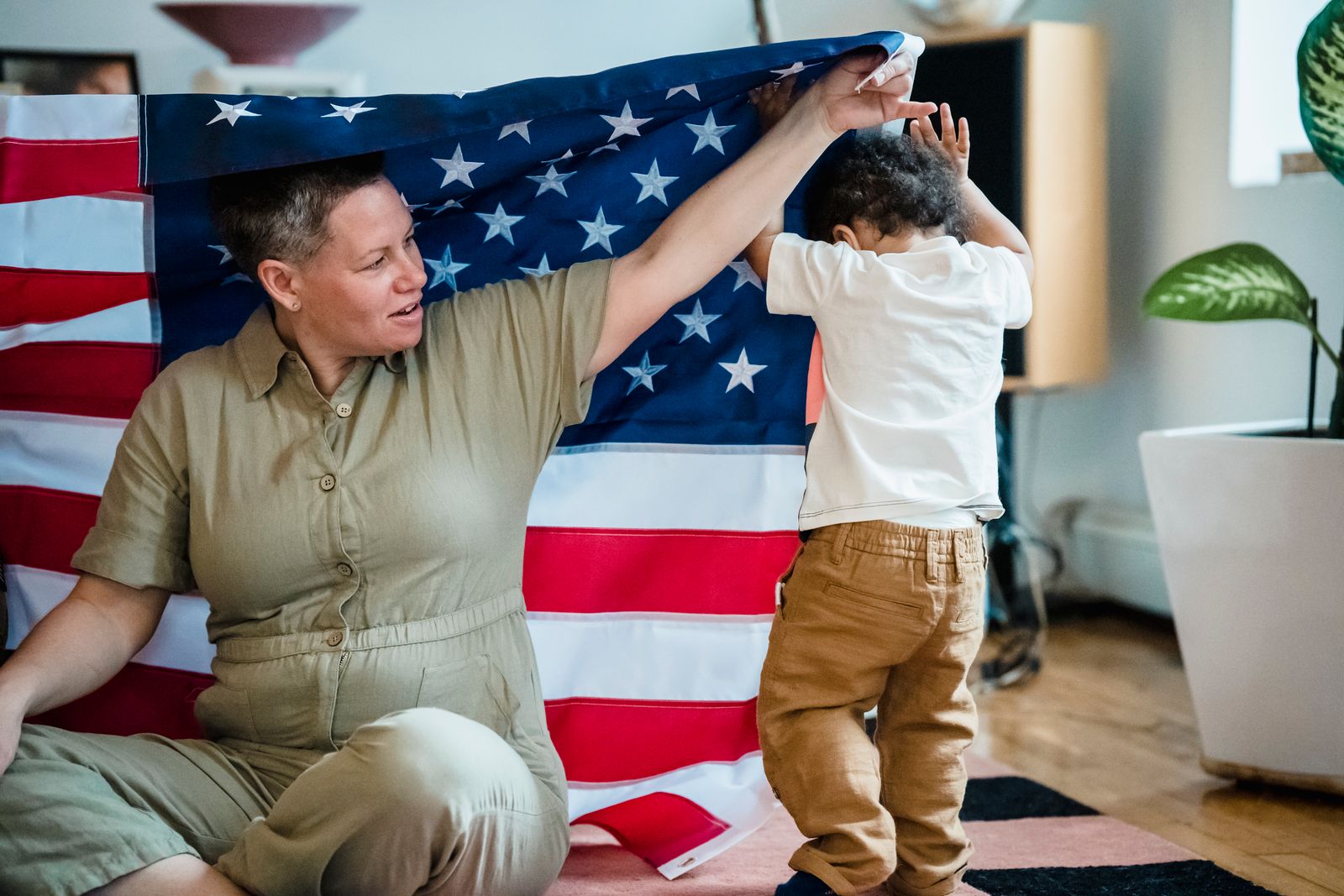 A mother and her young child playing together beneath a large American flag in their home