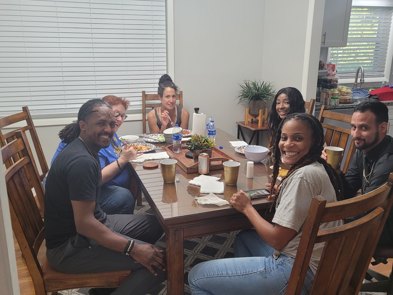 Real people laughing together around a dinner table at an SMS Novel home gathering